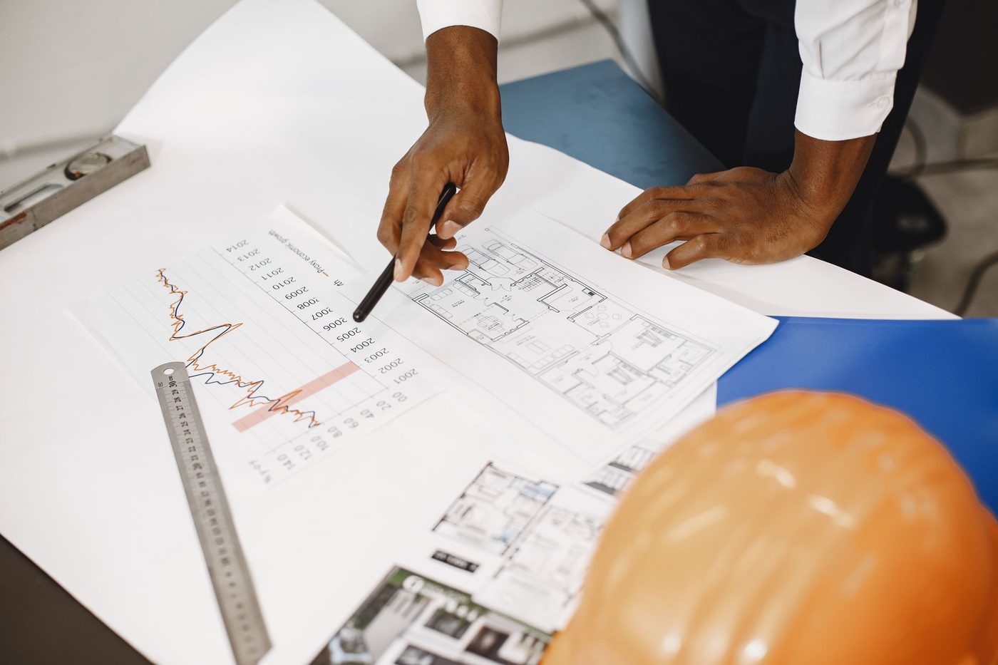 Hands reviewing house floor plan blueprints beside a hard hat and ruler