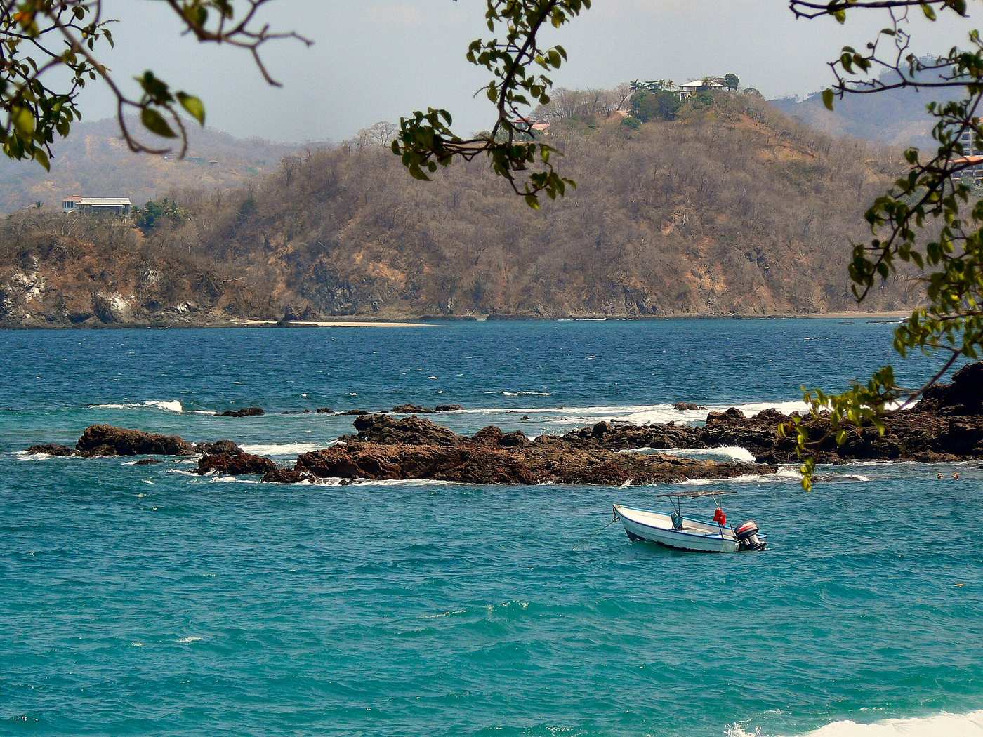 Turquoise water and rocky shoreline at Playa Conchal with homes on the hills above