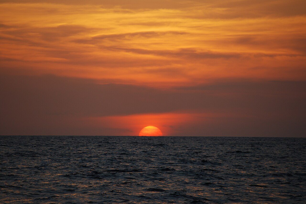 Fiery orange sun setting over calm ocean waves at Playas del Coco